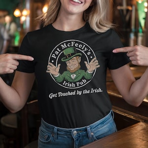 May include: Black t-shirt with a white circle graphic featuring a cartoon leprechaun with a green hat and the text "Pat McFeely's Irish Pub" and the text "Get Touched by the Irish."