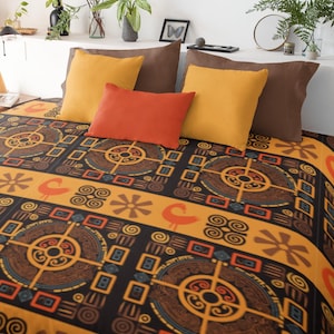 Puede incluir: Una cama con una manta estampada y almohadas. La manta presenta un diseño repetitivo en negro, naranja y marrón. Las almohadas son en tonos marrones, naranjas y amarillos. La cama está contra una pared blanca con plantas y objetos decorativos.