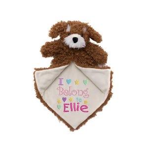 May include: A brown plush dog toy with a white muzzle and a cream-coloured blanket. The blanket has the embroidered text "I Belong to Ellie" with colourful hearts and stars. The toy is designed for babies and young children.