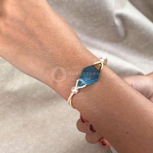 May include: A white string bracelet with a blue and gold gemstone charm and white pearl accents.