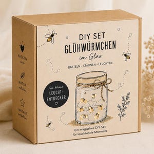 Könnte beinhalten: Eine braune Pappschachtel mit der Aufschrift "DIY SET GLÜHWÜRMCHEN im Glas". Die Illustration zeigt ein Einmachglas mit Glühwürmchen. Die Box enthält auch den Text "Für kleine LEUCHT-ENTDECKER" und Zeichnungen von Bienen.