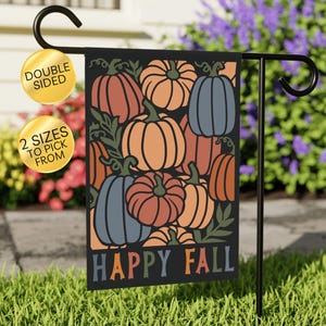 May include: A double-sided black garden flag featuring a colorful pumpkin design with orange, blue, and rust-colored pumpkins. The words "HAPPY FALL" are at the bottom. The flag is displayed on a black metal stand.