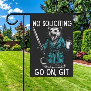 Pode incluir: Uma bandeira de jardim preta com o texto "NO SOLICITING" e "GO ON, GIT". A bandeira apresenta uma ilustra&ccedil;&atilde;o de um gamb&aacute; em um roup&atilde;o verde-azulado segurando uma espada e uma x&iacute;cara de caf&eacute;. A bandeira &eacute; exibida em um suporte de metal preto.