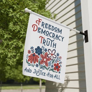 May include: A white flag with the words "Freedom, Democracy, Truth, and Justice for All" in navy blue and red lettering. The flag features a floral design with red, blue, and white flowers.