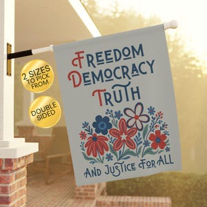 May include: A double-sided flag with the words "Freedom, Democracy, Truth, and Justice for All" in blue and red lettering. The flag features a floral design with red and blue flowers. The flag is displayed outdoors.