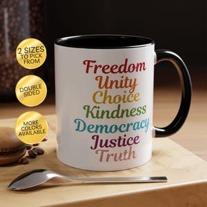 May include: A white ceramic mug with a black interior and handle. The mug features the words "Freedom, Unity, Choice, Kindness, Democracy, Justice, Truth" in rainbow colors. Additional text on the mug includes "2 Sizes to Pick From", "Double Sided", and "More Colors Available".