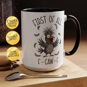 May include: White ceramic mug with a black handle and rim, featuring a cartoon crow illustration and the text "FIRST OF ALL F-CAW-F". The mug has a double-sided design and is available in multiple colors.