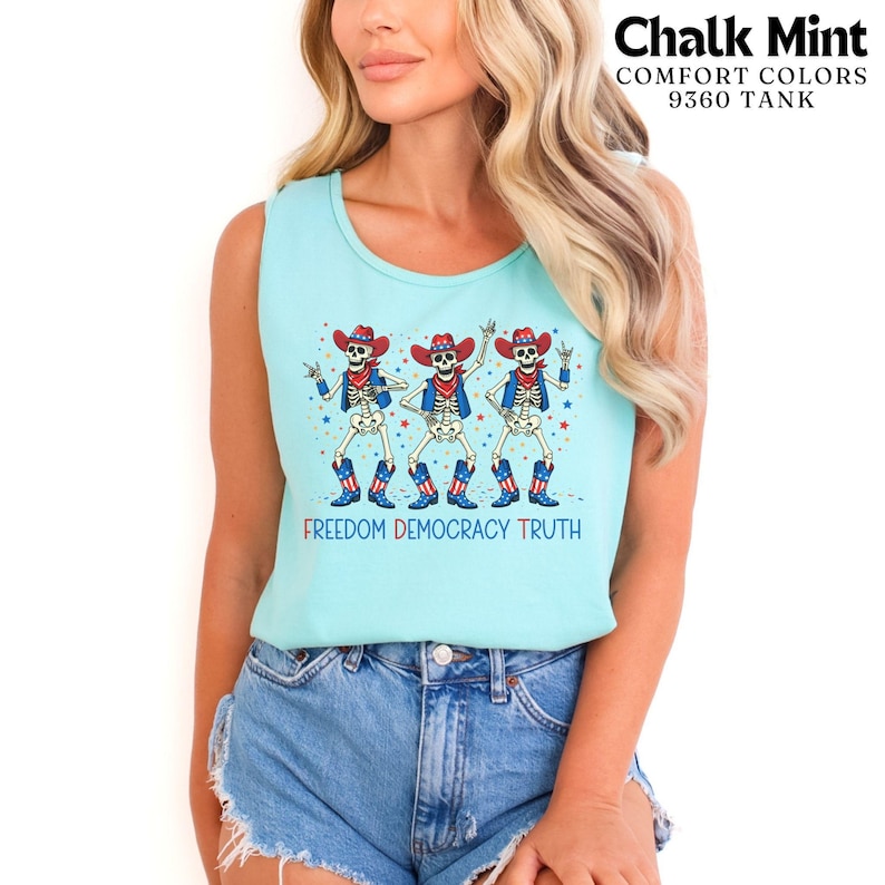 May include: A light mint green tank top featuring a graphic of three skeletons wearing red, white, and blue cowboy hats, vests, and boots. The text "FREEDOM DEMOCRACY TRUTH" is printed below the skeletons, with small stars scattered around them.