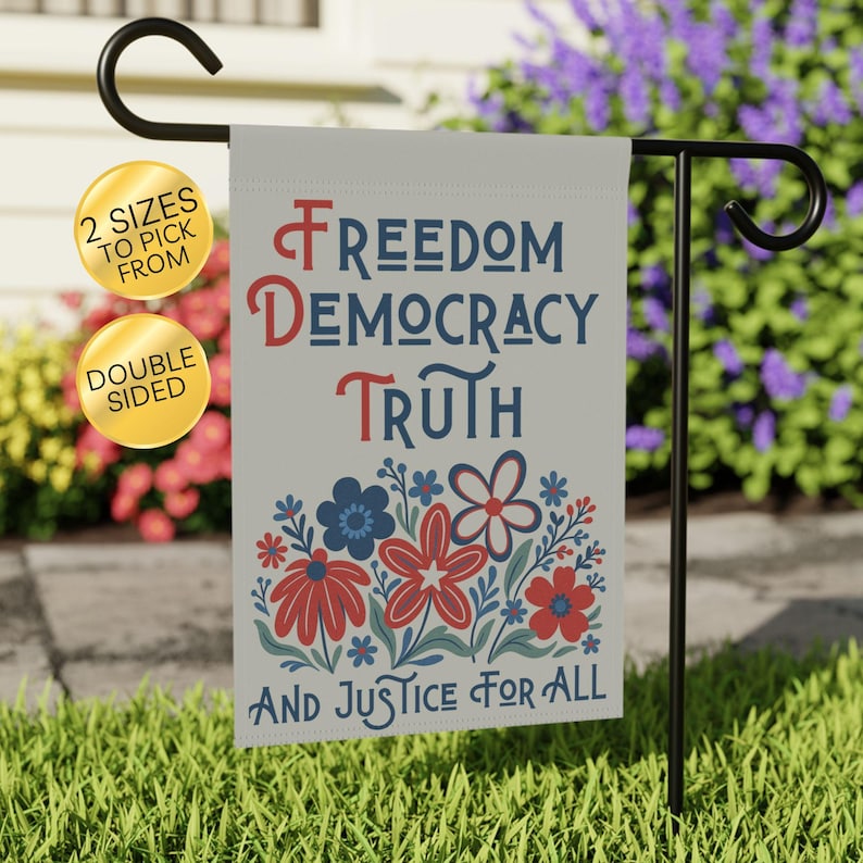 May include: A double-sided garden flag with patriotic text and floral design. The flag displays the words 'Freedom, Democracy, Truth, and Justice For All' in red and blue. A floral pattern of red and blue flowers is at the bottom. The flag is hanging on a black metal stand.