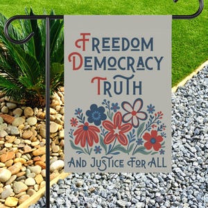 May include: A garden flag with the words "FREEDOM DEMOCRACY TRUTH" in red and blue, with a floral design below and the words "AND JUSTICE FOR ALL". The flag is displayed on a black metal stand.