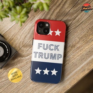 May include: A red, white, and blue phone case with the text "FUCK TRUMP" in bold white letters. The case has two white stars on the red section and three white stars on the blue section. A gold sticker says "MORE SIZES AVAILABLE".