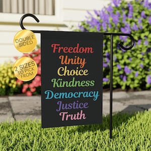 May include: A black garden flag with the words "Freedom, Unity, Choice, Kindness, Democracy, Justice, Truth" in rainbow colors. The flag is double-sided and available in two sizes. It is displayed on a black metal garden stake.