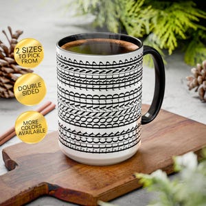 May include: A white ceramic mug with a black interior and handle, featuring a repeating black text pattern of the name Donald Trump arranged in horizontal bands around the exterior. The mug has a cylindrical shape and a curved handle on the side.