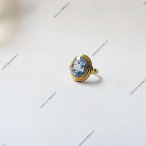 Könnte beinhalten: Ein goldener Ring mit einem hellblauen ovalen Edelstein, der in einer Zargenfassung sitzt.