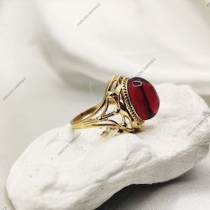 Könnte beinhalten: Ein goldener Ring mit einem roten ovalen Edelstein, der in einem dekorativen Filigranmuster gefasst ist.