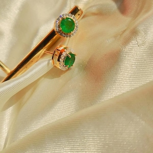 Puede incluir: Un par de pendientes de oro con piedras preciosas verde esmeralda rodeadas por un halo de diamantes más pequeños.