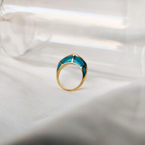 Könnte beinhalten: Ein goldener Ring mit einem türkisblauen Stein, der in einem geometrischen Design gefasst ist.