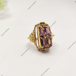 May include: A gold ring with a rectangular amethyst gemstone set in a bezel setting. The ring has a delicate, ornate design.