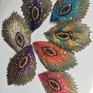 Op de afbeelding: Een verzameling van zes geborduurde veer-vormige patches met gedetailleerde gouden draadaccenten en centrale lovertjes. De patches zijn uitgevoerd in diverse levendige kleuren, waaronder blauw, zilver, paars, oranje, roze en meerkleurig.