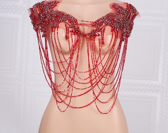 May include: Red beaded and sequined shoulder piece with a chain-like design. The piece is made of red beads and sequins and has a chain-like design. It is worn on the shoulders and hangs down the front of the body.