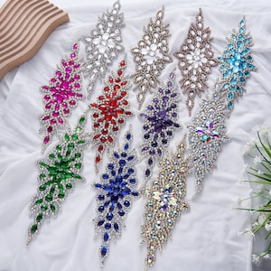 May include: Assortment of 10 rhinestone embellishments in various colours, including clear, turquoise, purple, green, red, blue, and iridescent. Each embellishment features a cascading design with multiple tiers of rhinestones.