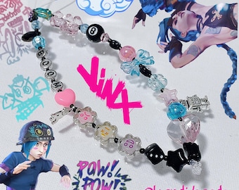 Könnte beinhalten: Ein farbenfrohes Perlenarmband mit einem rosa Herz, silbernen Charms und schwarzen Perlen. Das Armband hat außerdem einen blauen und rosa Schleifen-Charm, einen silbernen Roboter-Charm und eine schwarze Perle mit einer weißen Acht. Das Armband liegt auf einem weißen Hintergrund mit dem Text "@kendi.beads" und "POW! POW! POW!" in rosa und schwarz.