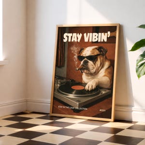 Może przedstawiać: Oprawiony wydruk przedstawiający buldoga w okularach przeciwsłonecznych palącego cygaro, z napisem "STAY VIBIN'". Pies znajduje się za gramofonem. Wydruk jest częścią "STAY IN THE LOOP COLLECTION".