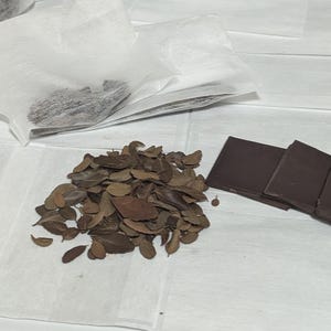 Puede incluir: Un montón de hojas marrones secas sobre una superficie blanca, junto a varias barras de chocolate negro.