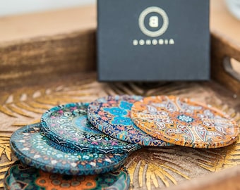 May include: Set of six colorful round coasters with intricate patterns. The coasters are made of a hard material and have a glossy finish. The coasters are arranged in a stack, with the top coaster featuring a bright orange and blue design.