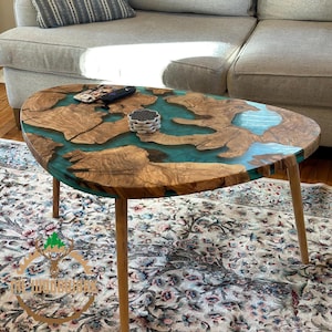 May include: A unique oval-shaped coffee table with a wooden base and a turquoise epoxy resin top. The table has four wooden legs and is sitting on a patterned rug.