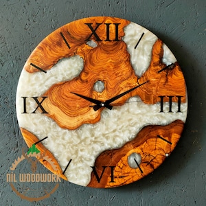 Può includere: Un orologio rotondo in legno con numeri romani e un'intarsio in resina epossidica bianca. Il quadrante dell'orologio presenta un motivo a venature del legno naturale e le lancette sono nere.