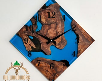 May include: A square clock with a blue resin face and a wood inlay. The clock face has black numbers and hands. The wood inlay is a dark brown color with a natural wood grain pattern.