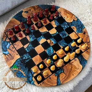 May include: A round wooden chessboard with a blue and brown epoxy resin design. The board has black and white squares and is numbered with letters and numbers around the edge. There are red and yellow chess pieces on the board.