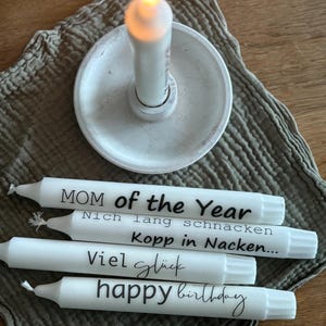 Könnte beinhalten: Vier weiße Kerzen mit schwarzem Text. Die Kerzen sagen "MOM of the Year", "Nich lang schnacken", "Kopp in Nacken...", und "Viel glück happy birthday".