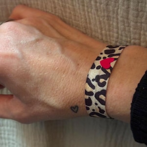 Puede incluir: Una pulsera elástica de leopardo marrón y negro con un dije de corazón rojo.
