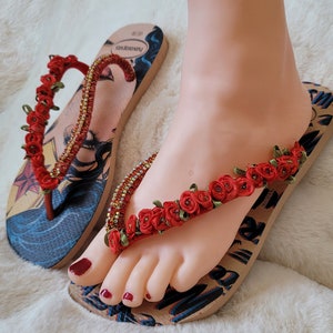 May include: A pair of brown flip-flops with a Wonder Woman graphic and red flower embellishments.