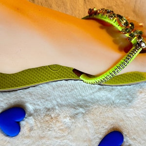 May include: Lime green flip flops with a rhinestone and green beaded strap. The strap has a large, clear rhinestone in the center.