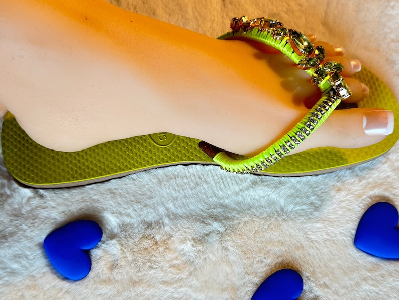 May include: Lime green flip flops with a rhinestone and green beaded strap. The strap has a large, clear rhinestone in the center.