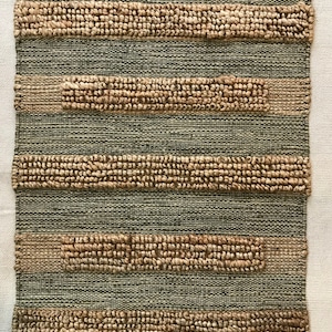 May include: A green and brown woven rug with a fringed edge. The rug has a striped pattern with alternating bands of green and brown.