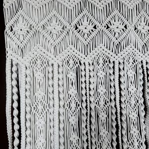 Peut inclure: Suspension murale en macramé blanche avec un motif géométrique et des franges. La suspension est en cordon de coton et a un style bohème.