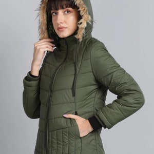 Könnte beinhalten: Eine grüne Steppjacke mit einer Kapuze, die mit Kunstfell gefüttert ist. Die Jacke hat einen Reißverschluss und zwei Taschen.