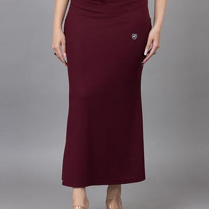 May include: A burgundy slip skirt with a drawstring waist. The skirt has a small white logo on the right side. The model is wearing clear heeled sandals. This skirt is suitable for layering under a saree or other garments.