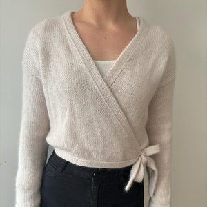 May include: A light beige wrap cardigan with long sleeves and a tie at the waist.