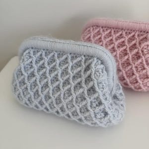 Peut inclure: Deux petites pochettes au crochet avec une fermeture à fermoir métallique. L'une est bleu clair et l'autre rose clair. Les deux présentent un motif en losanges en relief sur toute la surface extérieure, réalisé avec des mailles épaisses.