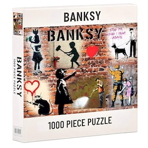 Könnte beinhalten: Ein 1000-teiliges Banksy-Puzzle mit verschiedenen ikonischen Streetart-Bildern. Die Box zeigt eine Collage von Kunstwerken, darunter ein Mädchen, das eine Bombe umarmt, ein Junge mit einem Hammer und eine Ratte mit einer Sprühdose. Das Puzzle ist in einer weißen Box verpackt.