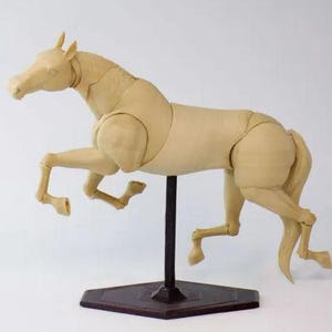 Op de afbeelding: Een beige, beweeglijk paardenmodel in een dynamische pose, gemonteerd op een zwarte standaard met een bruine basis. De gewrichten van het model zijn zichtbaar, wat duidt op een anatomische studie of animatiereferentie. Het paard wordt in volle gang afgebeeld.