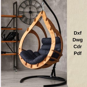 Puede incluir: Silla colgante de madera con diseño de lágrima. La silla tiene un acabado de madera natural y un cojín azul oscuro. Está suspendida de un marco de metal negro. La imagen también incluye el texto "Dxf Dwg Cdr Pdf".