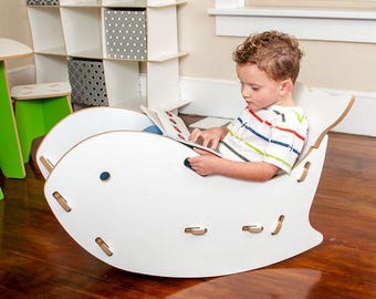 Peut inclure: Une chaise berçante en bois blanc en forme de poisson. Un enfant est assis dans la chaise et lit un livre.