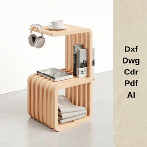 Puede incluir: Una mesa auxiliar de color madera clara con un diseño curvo único. La mesa tiene dos estantes, con libros, una manta doblada y una taza de café con auriculares. La mesa mide aproximadamente 61 cm de altura.