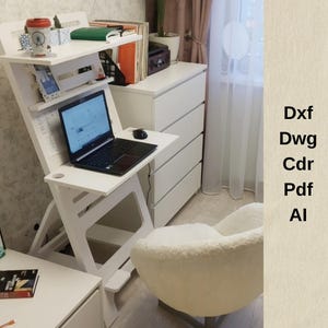 Op de afbeelding: Witte staande bureau met een laptop, muis en boeken op de planken. Het bureau staat in een kamer met een witte stoel en een witte commode.